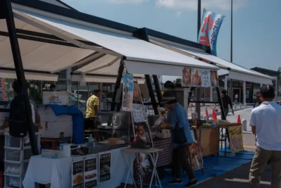 Imagem de um mercado ao ar livre com estandes variados, destacando a diversidade de produtos e comidas. Ideal para montadoras de stands que buscam inspiração.