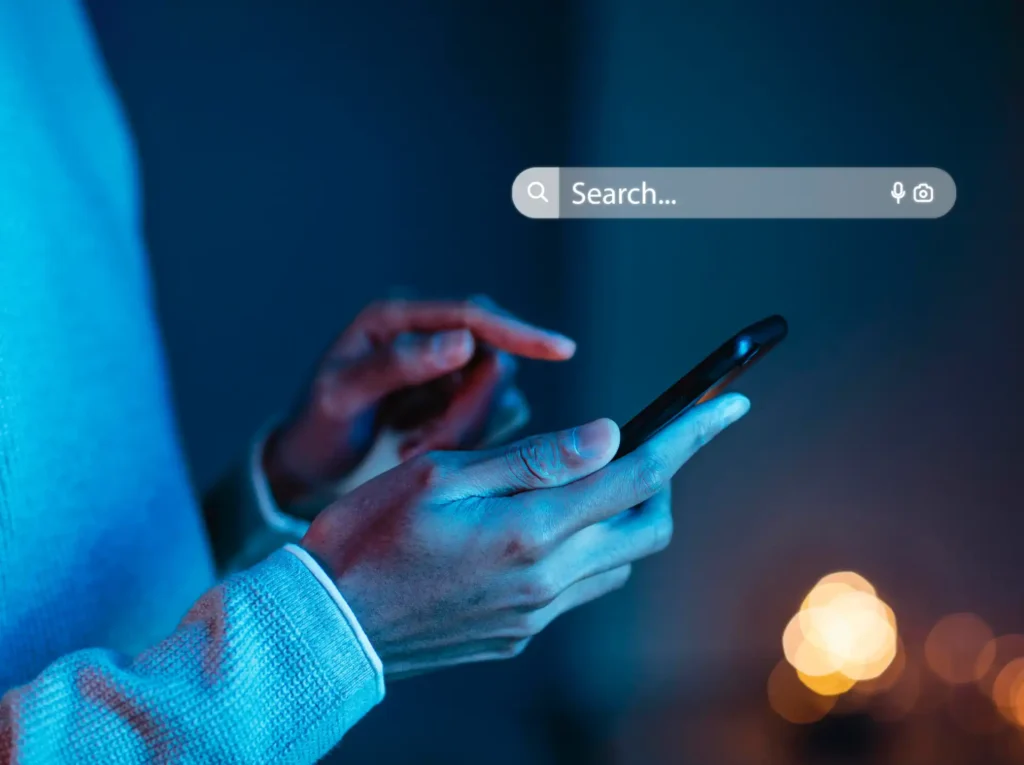 Imagem de um usuário utilizando um smartphone em ambiente escuro, com foco na busca por Sitemap XML. A imagem destaca a interação digital e a tecnologia.