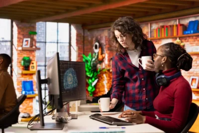 Duas profissionais de marketing discutindo estratégias de uso de ferramentas de IA em um ambiente de escritório moderno, promovendo inovação em 2025.